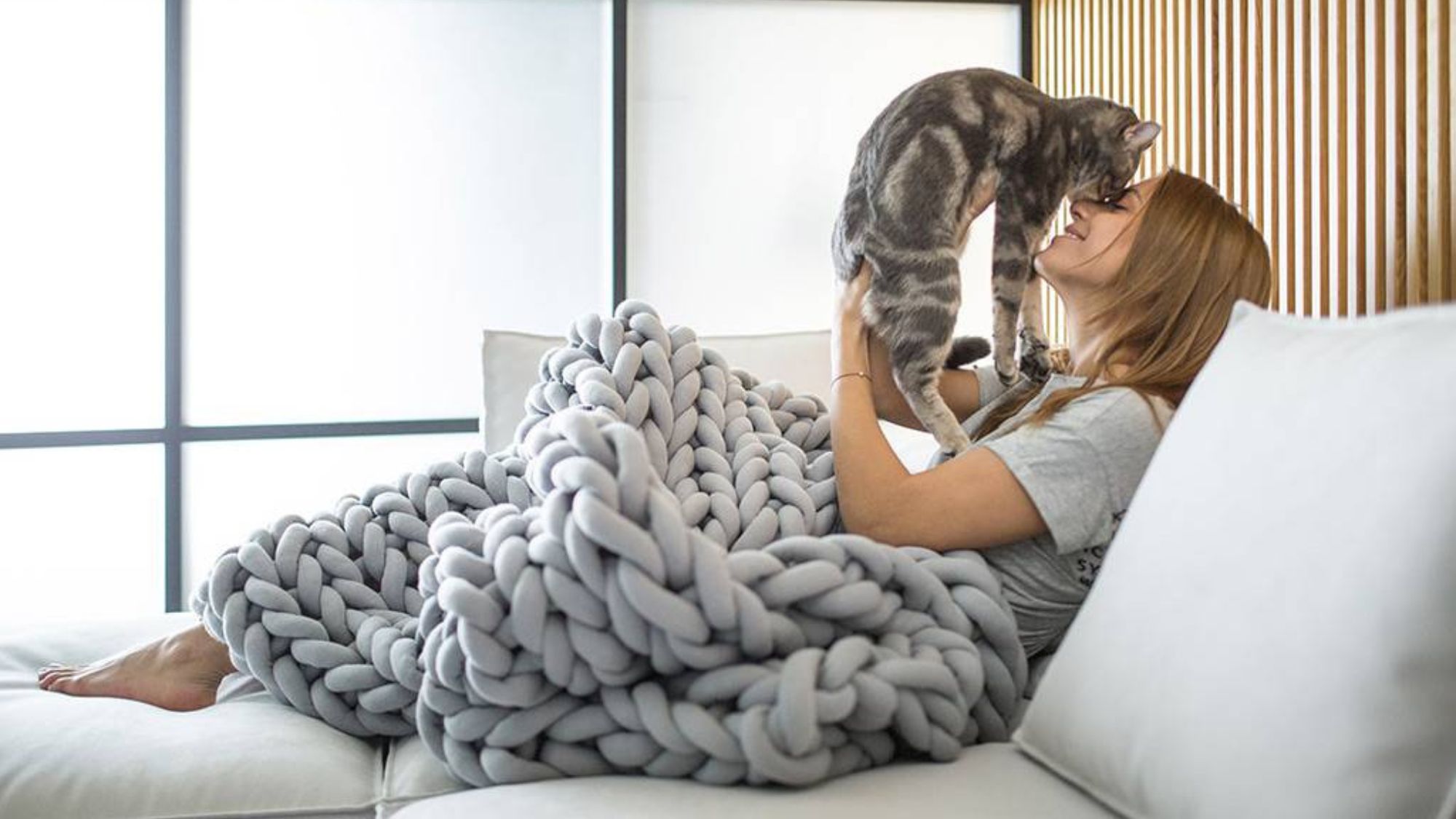 A girl playing with a cat laying in a bed with cosy blankets